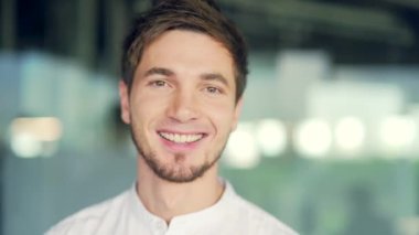 Close-up portrait of young caucasian man looking at camera smiling. Head shot Handsome businessman standing in office. Successful happy male employee entrepreneur posing for recording video indoor