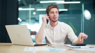 Smiling working man having phone conversation and using calculator at her office desk Businessman talking on phone in office Bookkeeper holding cellphone, making call to colleague or business partner