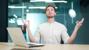 Young calm mindful man meditating doing yoga exercise sitting on the office, relax at work, peace of mind employee meditate at workplace Office worker, IT programmer resting from work with closed eyes