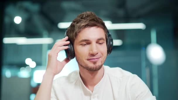 Χαμογελώντας Νεαρός Άνδρας Ακούγοντας Μουσική Ακουστικά Μάτια Κλειστά Ενώ Κάθεται — Αρχείο Βίντεο