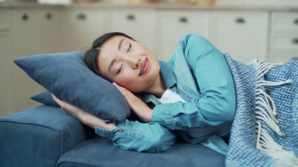 リビングルームのソファに横たわっている間 日中は毛布で覆われて寝ている若いアジアの女性のクローズアップ 家で快適なソファに横になっている間 かわいい女性は眠りに笑っています シエスタ — ストック動画