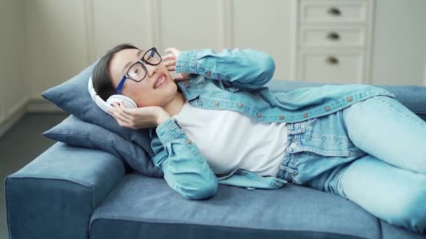 Young Asian Woman Wearing Headphones Listening Music While Lying Sofa — Vídeo de Stock