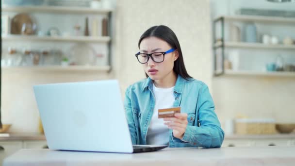 可悲的亚洲女人坐在家里的办公桌前 却在笔记本电脑上输入信用卡号码 结果没有成功 戴眼镜的年轻女性不高兴也不高兴 因为她在电脑上工作时犯了个错误 — 图库视频影像