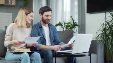 Accounting at Home Happy couple using laptop computer sitting on Sofa in house Family Filling Tax Forms, Mortgage Documents, Bills, Checks, Balances, Invoices are in Order satisfied and contented