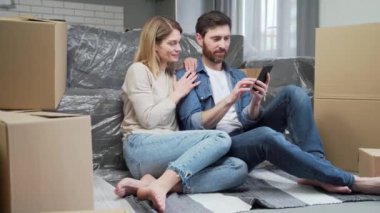 Gülümseyen evli çift daire dekorasyonunu planlıyorlar online mağazalara bakıyorlar yeni evlerinin oturma odasında oturuyorlar arka planda bir sürü kutu var taşınma konsepti