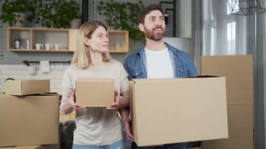Portrait happy married couple moves into a new apartment. Adult joyful man and woman enter the kitchen holding cardboard boxes in their hands They are satisfied, look around the room hug and smile