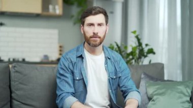 Mature caucasian man looking at camera and listens talking sitting on sofa at home. Webcam view of confident bearded male having conversation with virtual meeting interlocutor, gesturing with hands