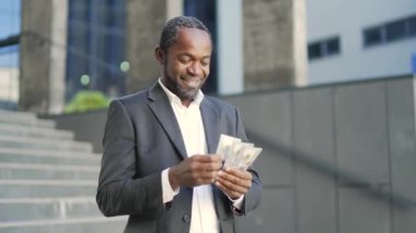 Mutlu Afro-Amerikalı olgun bir adam dışarıda ofis binasının önünde dolar sayıyor. Resmi takım elbiseli orta yaşlı bir işadamı elinde para tutuyor ve iyi kazançlardan zevk alıyor.