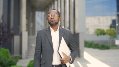 Gözlüklü, kameraya bakan kendinden emin Afro-Amerikan olgun profesörün portresi. Resmi takım elbiseli orta yaşlı bir adam elinde klasörle bir üniversite binasının önünde duruyor.