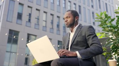 Kulaklıklı, dışarıda dizüstü bilgisayar kullanan kendine güvenen Afro-Amerikalı olgun bir adam. Resmi takım elbiseli ciddi bir orta yaşlı erkek işadamı bir bankta oturur ve bir ofis binasının arka planında yazar.