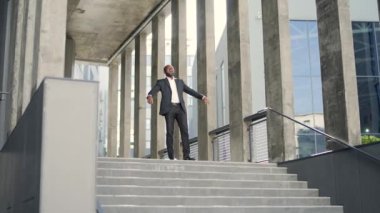 Mutlu Afro-Amerikan iş adamı zaferi ofis binasının önünde kutluyor. Resmi takım elbiseli bir adam ellerini muzaffer bir jestle kaldırır. Başarılı bir iş anlaşması.