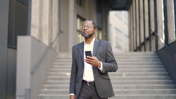 Улыбающийся Африканский Американский Бизнесмен Проверяет Текстовые Сообщения Держа Руках Смартфон — стоковое видео