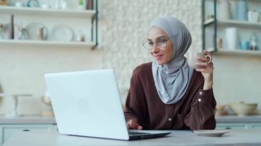Young Muslim woman in hijab in love communicates on a dating site Smiling female laptop computer feel satisfied Pretty girl lifestyle Concept relationships online communication at home Remote chat