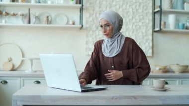 Young Muslim woman with poisoning or intoxication feels bad. A female in a hijab suffers from nausea and vomiting while working at home on a laptop computer. indoor Unhealthy pregnancy syndrome