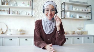 Webcam view of business coach talking by video conference in the living room Young confident Muslim woman wear wireless headset looking at the camera businesswoman having online meeting at home 