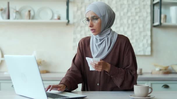 若いイスラム教徒の女性の肖像画は 自宅で台所に座っている鼻水とアレルギーのくしゃみに苦しんでいます不健康な女性気分悪いUnwell咳風邪やインフルエンザ室内だけでラップトップで仕事 — ストック動画