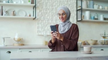 Mutlu gülümseyen bir kız telefonda mesaj yazarken evde oturan aşık genç bir kadın, internet üzerinden akıllı telefon kullanarak sosyal ağda erkek arkadaşı veya arkadaşıyla sohbet ediyor.