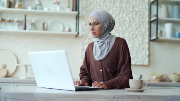 眼鏡をかけたヒジャーブの匿名のイスラム教徒の女性は ラップトップコンピュータに問題があることに不満を感じていますシステムエラーデータ損失のバックアップバッテリーの問題が自宅でパスワードを忘れたため 動揺した女の子は動作できません — ストック動画