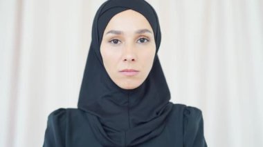 Yakın plan bir portre. Siyah tesettürlü, ciddi bir müslüman kadın. Evinde dikiliyor.