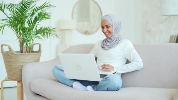 ヒジャーブ州の若いイスラム教徒の女性正の女性のフリーランスや学生がノートパソコンでビデオ通話で話していますリモートコミュニケーション会議自宅でビジネス女性が会話をしています — ストック動画