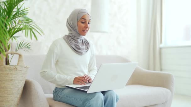 ヒジャーブ州の若いイスラム教徒の女性ビジネス女性がオンラインで会話をしている女性のフリーランスや家庭でのノートパソコンのリモート通信会議でビデオ通話で話す先生 — ストック動画