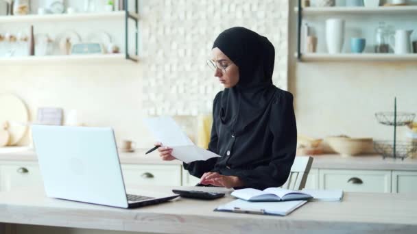 若いイスラム教徒の女性は オンラインで家庭から仕事を計算したり リモートで勉強しますヒジャーブの女性はノートパソコンを使用してコンピュータノートビジネス女性は アプリやウェブサイトを使用して個人的な財政を管理します — ストック動画