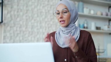 Muslim woman in hijab with eyeglasses look at camera, greeting and talk to colleagues or student by video call online meeting conference, chat, remotely at home teacher education studies