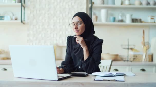 ノートパソコンを使ってノートパソコンでノートを取る若いイスラム教徒の女性は オンラインで遠隔学習し ビデオコースや電話を見て 自宅でEラーニングを勉強するヒジャーブの女性学生 — ストック動画