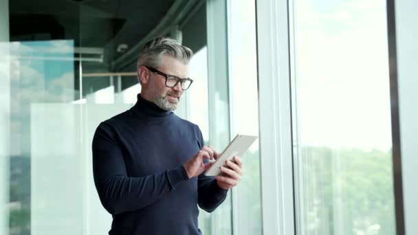 Mature Gray Haired Bearded Man Wearing Glasses Uses Tablet While — Stockvideo