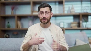 Webcam view of handsome bearded man with glasses looking at camera greeting and talking by video call online conference meeting or record content for social media at home Remote conversation chat