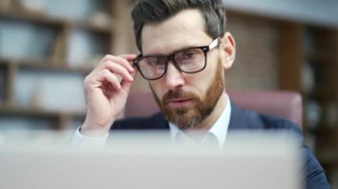 Close up portrait of busy mature business man with glasses typing on laptop computer working online at desktop in the office Concentrated entrepreneur takes responsible approach to the project indoors