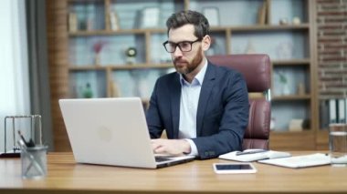 Busy mature business man investor with glasses typing on laptop computer working online at desktop in modern office Concentrated bearded entrepreneur takes responsible approach to the project indoors