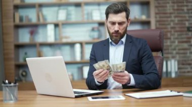 Konsantre sakallı iş adamı modern ofisteki masalarda dolar sayan banknotlar sayan ciddi bir girişimci elinde para tutan ve işyerindeki iyi kazançlara sevinen bir iş adamı.