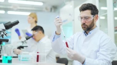 Medical researcher scientist asian man with protection holding blood sample HIV or bacteria testing in test tube and make experiment with colleagues at microbiology biochemistry hematology laboratory