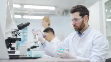 Koruması olan tıp araştırmacısı bilim adamı mikro biyoloji biyokimya laboratuvarında çalışan meslektaşlarıyla test tüpünde mavi kimyasal sıvı üzerinde deney yapıyor.