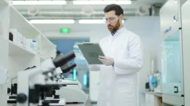 Portrait of concentrated mature man scientist with protective glasses and gloves working make notes descriptions and looking at the camera at microbiology pharmaceutical biochemistry laboratory indoor