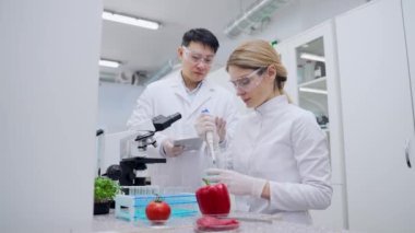 Medical researcher scientist woman make experiment dropping the chemical liquid while assistant writes results on digital tablet at microbiology biochemistry laboratory Diverse multiethnic team work