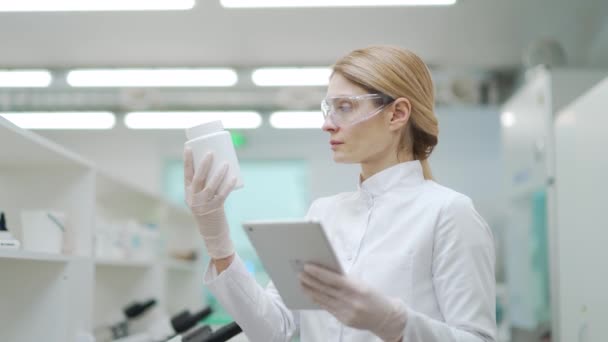 以成熟女科学家为研究对象 戴防护眼镜对药物药物进行研究 并与微生物学药物生物化学实验室的数字平板研究进行比较 — 图库视频影像