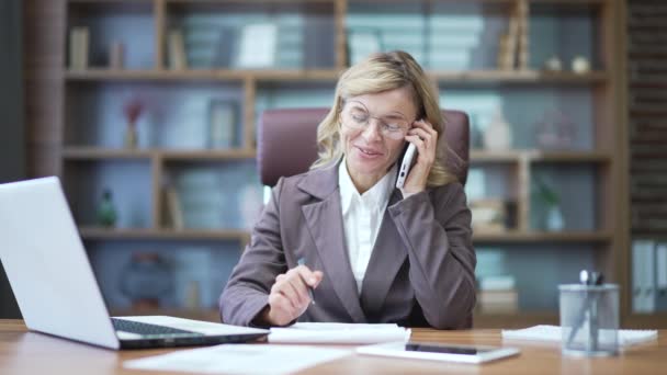 Mulher Negócios Madura Satisfeita Falando Telefone Enquanto Sentada Mesa Local — Vídeo de Stock
