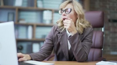 Overworked businesswoman tired from working with laptop. Mature worker is bored at work in the office. The employee cannot concentrate on work. Lazy woman procrastinating at the workplace, distracted