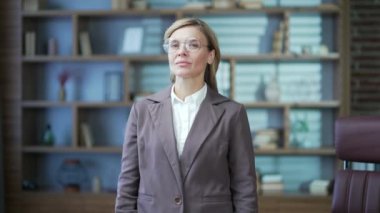 Portrait of smiling mature businesswoman in glasses and suit looking at camera while standing in office. Happy confident beautiful blonde female with crossed arms Head shot of a woman at the workplace