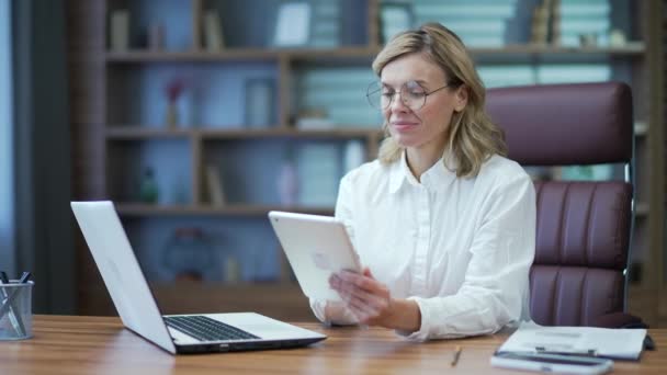Mature Businesswoman Glasses White Shirt Using Tablet While Sitting Desk — Stockvideo