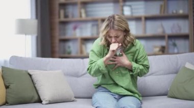 Allergic mature woman coughing because she has seasonal allergies sitting at home. First symptoms of cold and flu virus, pneumonia, bronchitis and respiratory tract infection. Seasonal virus disease