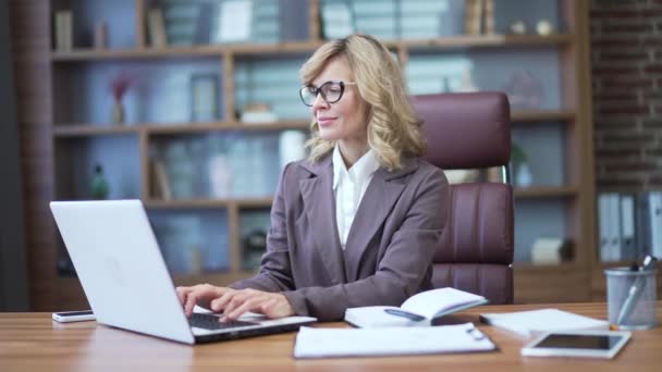Portrait Smiling Mature Businesswoman Suit Glasses Typing Laptop Desk Workplace — Stockvideo