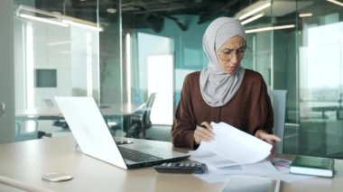 Endişeli, tedirgin, tesettürlü genç Müslüman iş kadını, modern ofiste evrak işleriyle ilgili sorunlar yaşıyor. Stresli kadın çalışanlar, iş yerlerindeki istatistik raporlarını analiz etmekten yorgun düşüyor.