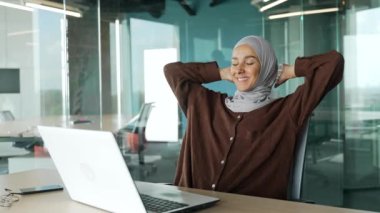 Smiling muslim businesswoman in hijab with hands behind head feels satisfied with work well done Happy worker with glasses relax after hard working day finished project on computer at modern workplace