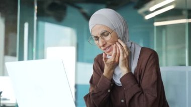 Stressed muslim businesswoman in hijab with severe toothache dental pain ache during computer work at office Sad worker suffering from discomfort because caries gum disease or sensitive teeth indoors