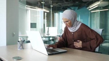 Sick young muslim businesswoman suffering from stomach ache during computer work holding belly feeling gastritis or abdomen colon pain at office workplace indoors Digestion poisoning problem concept