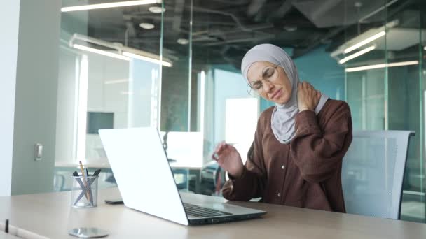 疲れた若いイスラム教徒のビジネスマンヒジャーブ州の女性は 現代の職場のデスクでラップトップコンピュータ上のハードワークから首の肩の筋肉の痛みに苦しんでいますOsteochonrosisコンセプト — ストック動画