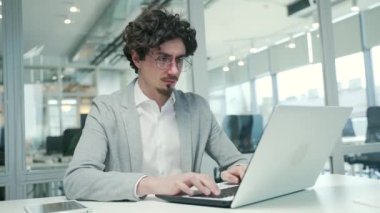 Tired overworked curly hair freelancer business man with eyes hurt massaging having bad poor vision after hard day working on laptop computer typing and browsing at desk in modern glass office indoors